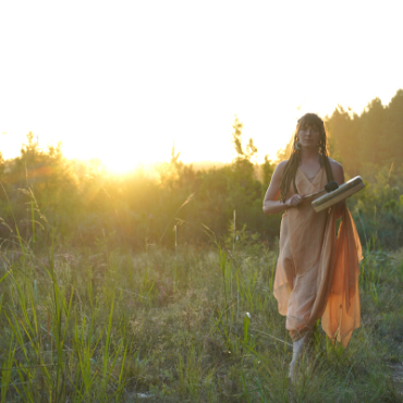 beautiful sunset forest fairy of Nature Theatre in the golden light sunlight playing ceremonial drum in hands with naked dress